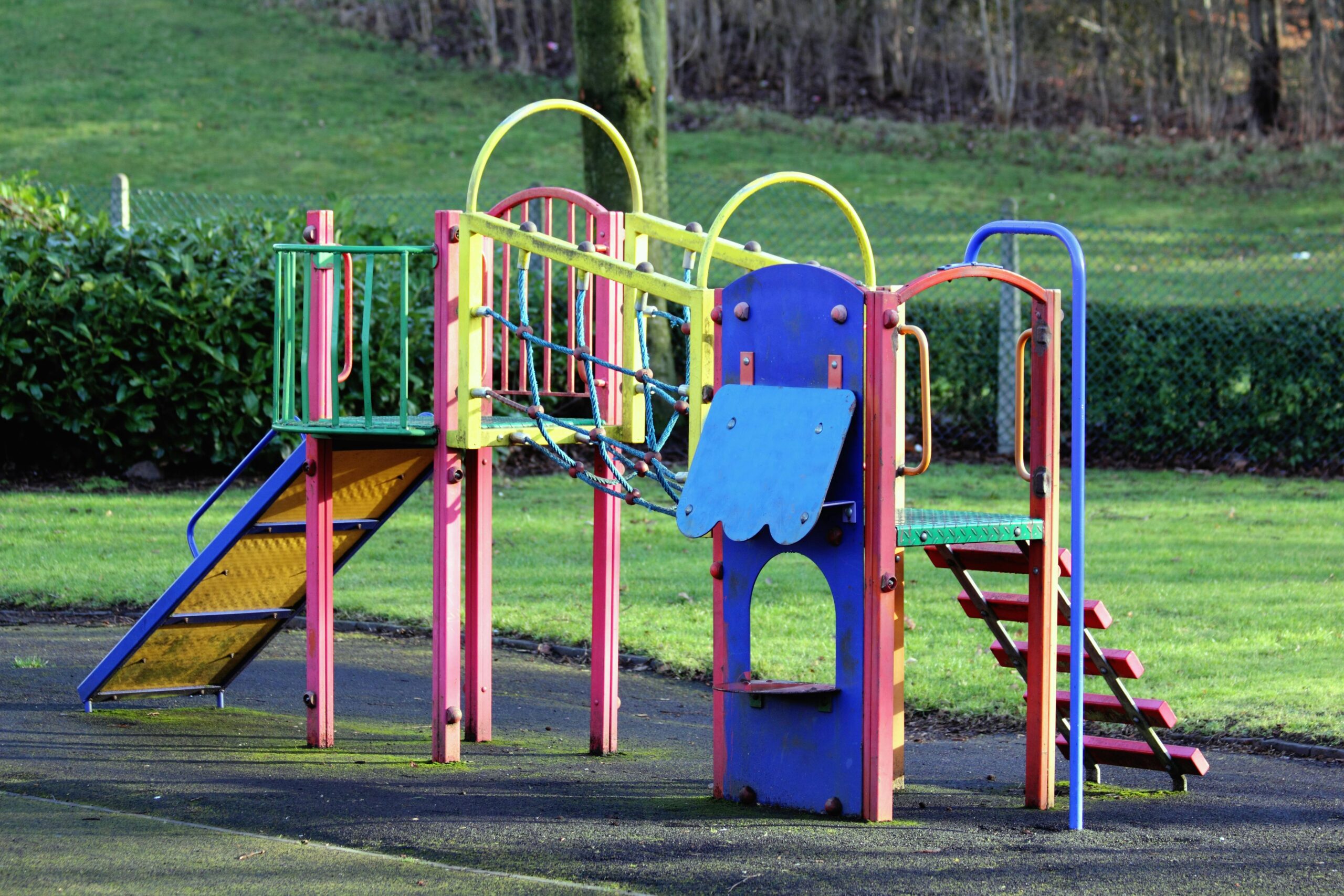 Vibrant playground equipment in an open park surrounded by grass and trees.